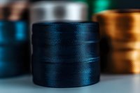 Dark blue sewing thread spool with textured surface pattern in macro photography against blurred background, showing fine detail of wound thread material.