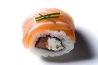 Fresh salmon sushi roll with cream cheese and chives garnish on white background, close-up view showing texture and layers of Japanese cuisine.