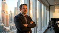 Confident middle-aged Caucasian businessman with crossed arms standing by office windows overlooking city skyline at sunset. Corporate executive portrait.