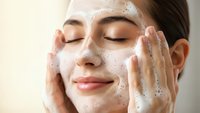 Young Asian woman applying foaming facial cleanser with gentle massage motions for daily skincare routine and healthy glowing skin care regimen.
