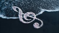 Treble clef symbol formed by ocean foam on dark beach sand, creating natural musical notation where sea meets shore.