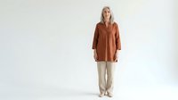 Caucasian woman with blonde hair wearing rust-colored linen shirt and beige pants, standing against white background for fashion and apparel design use.