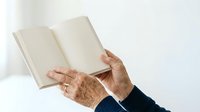 Senior woman with aged hands holding open blank book with cream pages against white background, suitable for education, literature, reading, and publishing concepts.