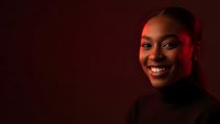 Young African American woman smiling warmly with professional lighting and red ambient glow against dark background for business and lifestyle content.