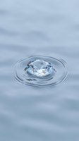 Crystal clear diamond floating on calm water surface creating gentle ripples in serene blue liquid environment for luxury jewelry concepts.