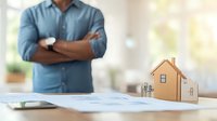 African American businessman with crossed arms reviewing real estate documents with miniature wooden house model on desk, soft natural lighting in modern office setting.