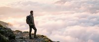 Male hiker with backpack standing on mountain peak above clouds at sunrise, adventure and exploration concept for travel and outdoor lifestyle.