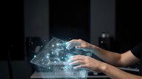 Hands interacting with futuristic holographic interface displaying glowing network connections and data visualization in modern digital workspace environment.