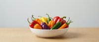 Colorful assortment of fresh chili peppers in a white bowl on a wooden table, showcasing vibrant red, yellow, green, and purple varieties.