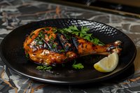 Glazed chicken leg quarter with honey-soy marinade served on black plate, garnished with fresh herbs and lemon wedge. Dark moody food photography.