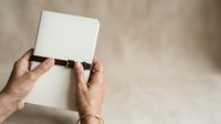 Close-up of mature adult hands holding blank white card against neutral beige background, suitable for business messaging, greeting card design, and promotional content.