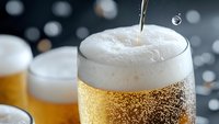 Fresh cold beer being poured into glass with frothy foam head and rising bubbles against dark background with bokeh lights. Close up macro photography.