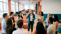 Professional blonde businesswoman leading team meeting in modern open office space with diverse group of colleagues discussing strategy and collaboration.
