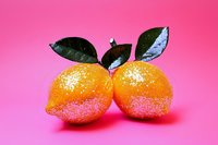 Fresh oranges with green leaves covered in water drops and sparkles on vibrant pink background, food photography for healthy lifestyle and citrus concepts.