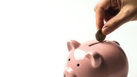 Hand inserting coin into pink piggy bank on white background for savings and financial planning concepts.