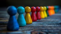 Colorful wooden game pieces lined up in diagonal row on rustic wood surface with selective focus and shallow depth of field creating artistic composition.