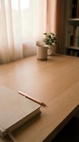 Minimalist workspace with copper pen on notebook at wooden desk. Soft natural light creates warm atmosphere for productivity and creative writing sessions.