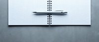 Open spiral notebook with grid paper and silver pen on gray surface for planning, note-taking, sketching, and office work organization.