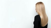 Young woman with long blonde hair wearing black top, viewed from side profile against white background, suitable for hair care and beauty marketing.