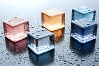 Colorful translucent ice cubes with water droplets on reflective surface for beverage and cooling concepts.