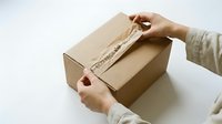Person with medium skin tone opening kraft cardboard box with tape, overhead view for shipping, delivery, and unboxing concepts.