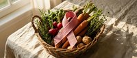Fresh organic vegetables and herbs in wicker basket on linen tablecloth by sunny window. Healthy farm produce including carrots, radishes and greens for cooking.