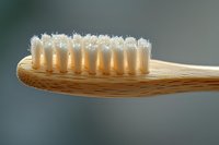 Close-up of eco-friendly bamboo toothbrush with white bristles against blurred background, showcasing sustainable oral hygiene product.