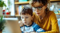 Young Caucasian mother with glasses and son using laptop together at home, family bonding through technology and digital learning activities.
