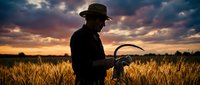 Farmer silhouette holding sickle in golden wheat field at dramatic sunset with stormy clouds for agricultural and harvest concepts.