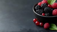Fresh raspberries, blackberries and red currants in black ceramic bowl on dark background with mint leaves, copy space for healthy food design.