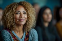 Confident young African American woman with curly blonde hair and bright smile wearing casual sweater, looking away thoughtfully in soft natural lighting.