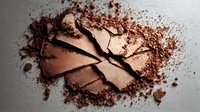 Crushed bronze eyeshadow or blush powder scattered on white surface, showing texture and pigment details for cosmetic product photography.