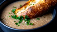 Creamy mushroom soup garnished with fresh parsley served in dark bowl with crusty toasted baguette slice, close up view of homemade comfort food.