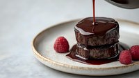 Decadent chocolate cake with glossy ganache drizzle and fresh raspberries on ceramic plate. Gourmet dessert photography for culinary and restaurant marketing.