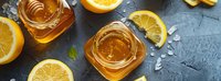 Golden honey in glass jars with fresh lemon slices on dark stone background, natural sweetener for tea and desserts.