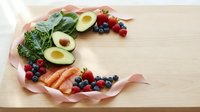 Fresh healthy foods arranged in crescent moon shape with salmon, avocado, berries and greens on wooden background for nutritious meal planning.