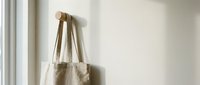 Natural cotton tote bag hanging on wooden wall hook in minimalist interior. Eco-friendly reusable shopping bag mockup for sustainable lifestyle branding.
