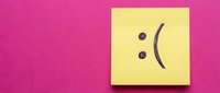 Yellow sticky note with sad face emoticon on bright pink background expressing disappointment and negative emotions for mental health concepts.