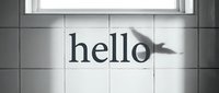 Hello text on white tiled wall with bird shadow and window light in black and white, minimalist greeting concept.