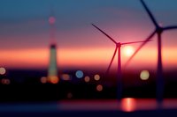 Wind turbines silhouetted against vibrant sunset sky with industrial lights and towers in background creating dreamy bokeh effect, renewable energy concept.