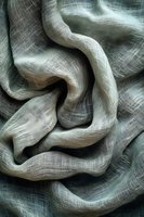 Soft flowing fabric with delicate textured lines creates elegant waves and folds in muted sage green tones, highlighting natural light and shadow patterns.
