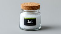 Glass jar filled with white sea salt crystals and cork lid on light gray background, minimalist kitchen storage container for cooking and seasoning.