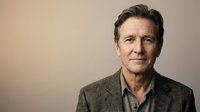 Middle-aged man with dark hair and facial stubble wearing casual gray blazer against neutral beige background, suitable for corporate portraits and professional headshots.