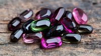Colorful tourmaline gemstones in pink, green and black shades scattered on rustic wooden surface, showcasing natural mineral crystals with faceted cuts and glossy finish.