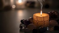 Burning candle with cracked wax surface surrounded by smooth stones creates peaceful spa atmosphere for relaxation and meditation practices.