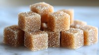Crystallized sugar cubes coated in fine granulated sugar create appetizing sweet texture, stacked in casual arrangement on white surface, macro food photography.