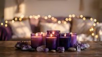 Purple candles burning with amethyst crystals creating cozy meditation atmosphere with warm bokeh lights on wooden table for relaxation and wellness.