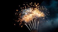 Spectacular golden fireworks display illuminating dark night sky with bright bursts and sparkling trails against smoky background.