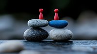 Minimalist zen stone arrangement with red wooden figures balanced on stacked pebbles, symbolizing harmony and connection in nature. Peaceful meditation concept.