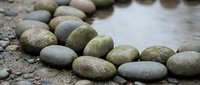 Smooth river stones arranged along water edge creating natural zen garden pathway for meditation and relaxation spa wellness design concepts.
